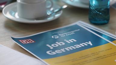 Ein Plakat mit der Aufschrift "Job in Germany" liegt bei einem Beratungsgespräch für aus der Ukraine Geflüchtete auf dem Tisch.